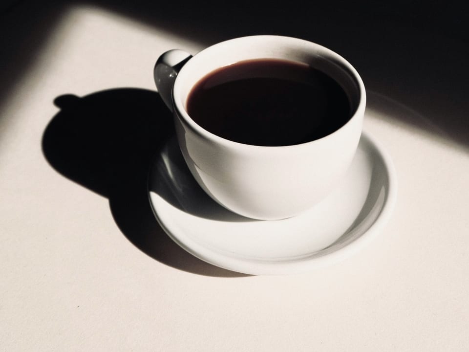 A cup of black coffee on a saucer in sunlight.